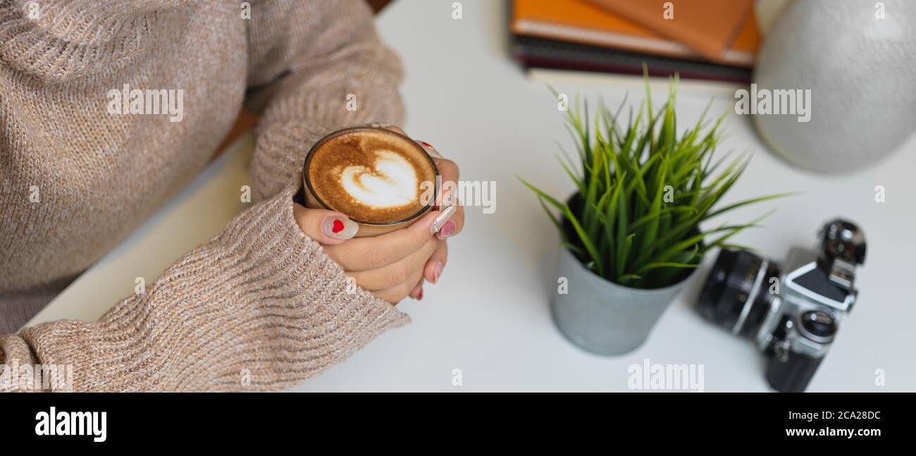 Side view of female in sweater hands holding a cup of coffee on table ...