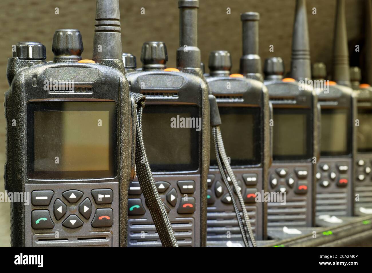 Black walkie talkies lined up in a row sitting upright on charging stations with focus on foreground. Stock Photo