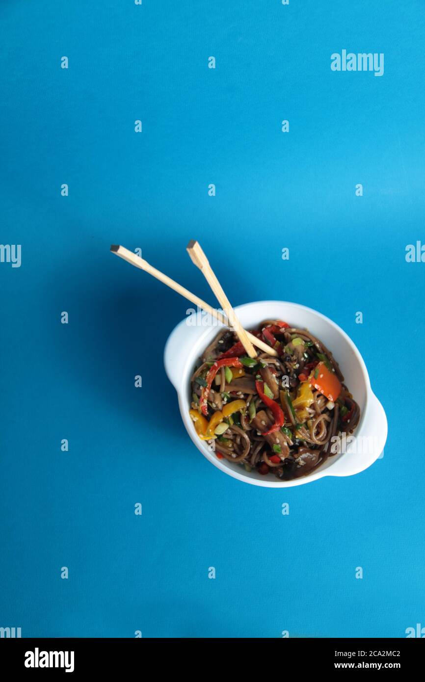 a bowl of wok noodles and chopsticks isolated on blue background flat lay. Image contains copy space Stock Photo