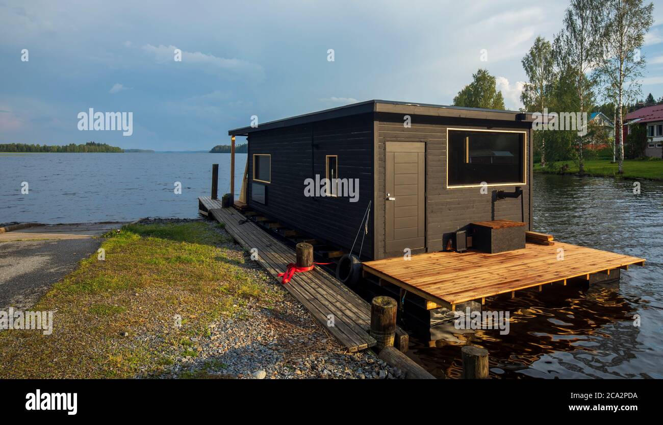 Floating brown wooden houseboat with sauna moored to jetty at lake