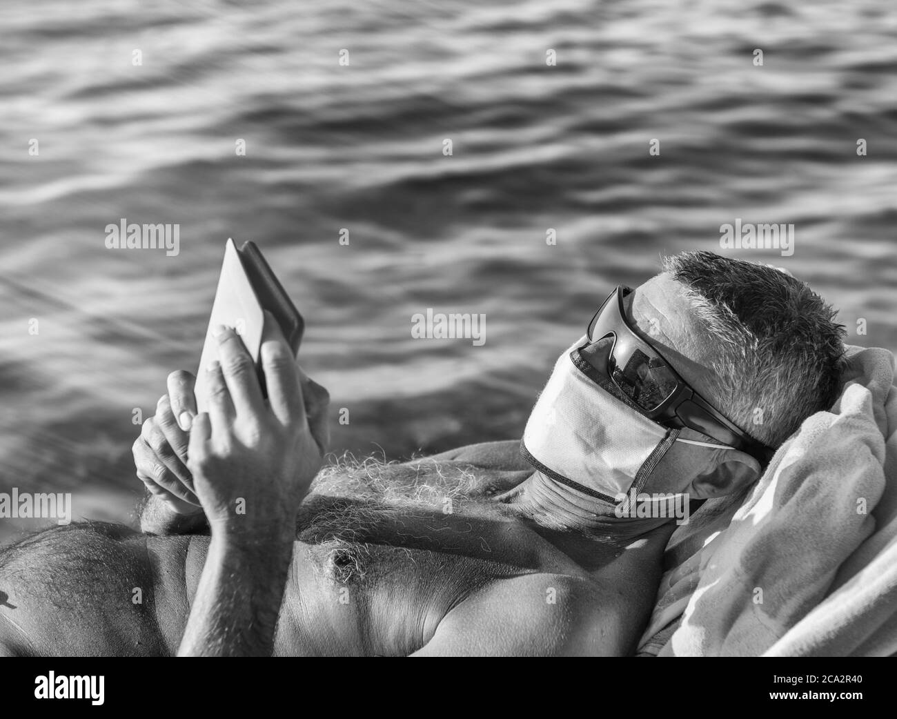 Man wearing mask and reading tablet on the beach in covid times. Stock Photo
