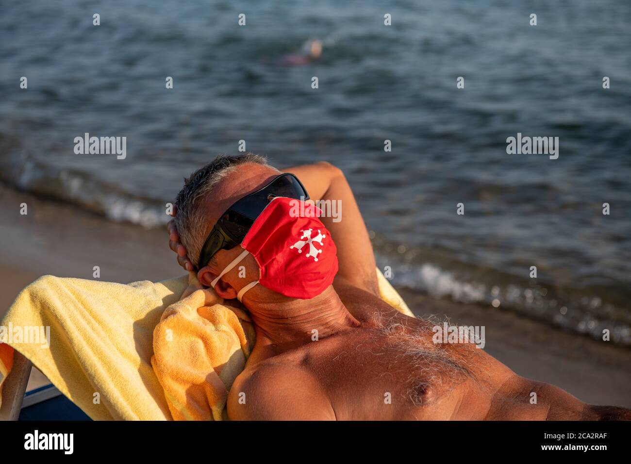 Man wearing mask lying on the beach in covid times Stock Photo