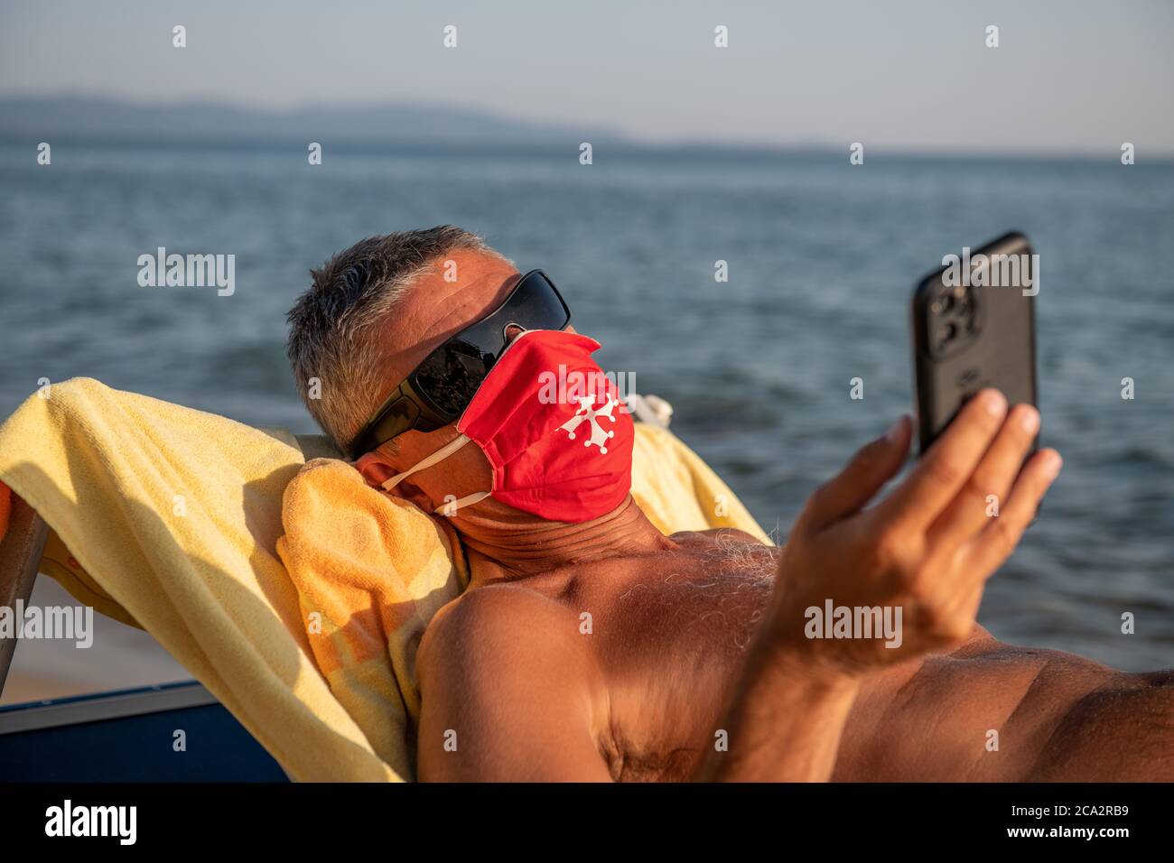 Man wearing mask and reading smartphone on the beach in covid times. Stock Photo