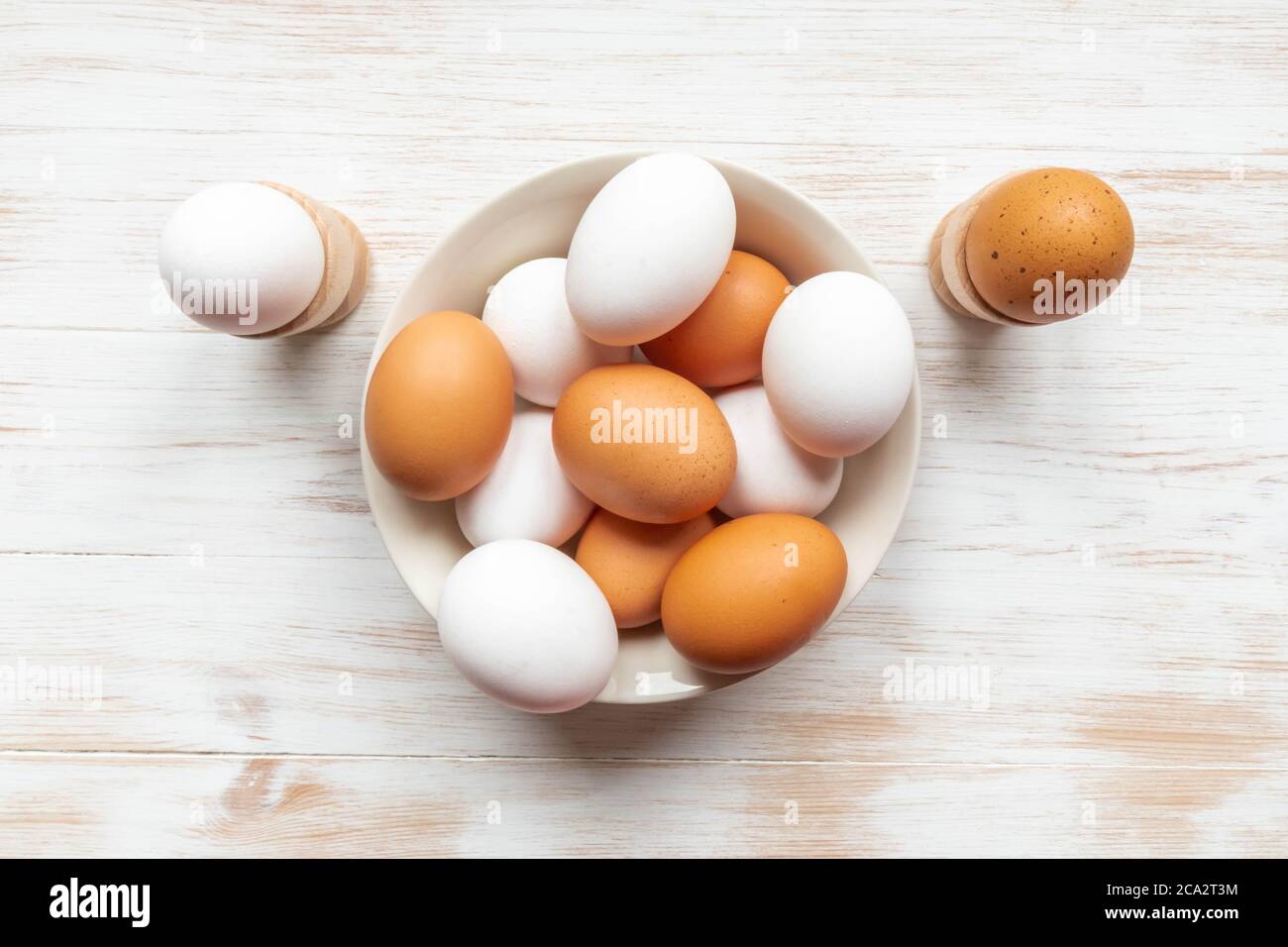 Bowl with brown and white chicken eggs on wooden table. Brown and white eggs in plate and holders on wood background. Free-range organic eggs. Flat la Stock Photo