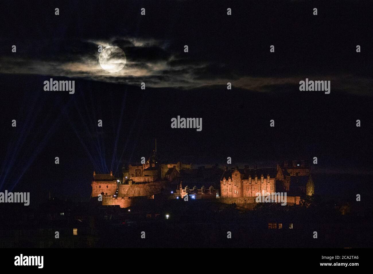 The full moon, known as a Sturgeon Moon in the month of August, rises through the clouds above Edinburgh Castle. Stock Photo
