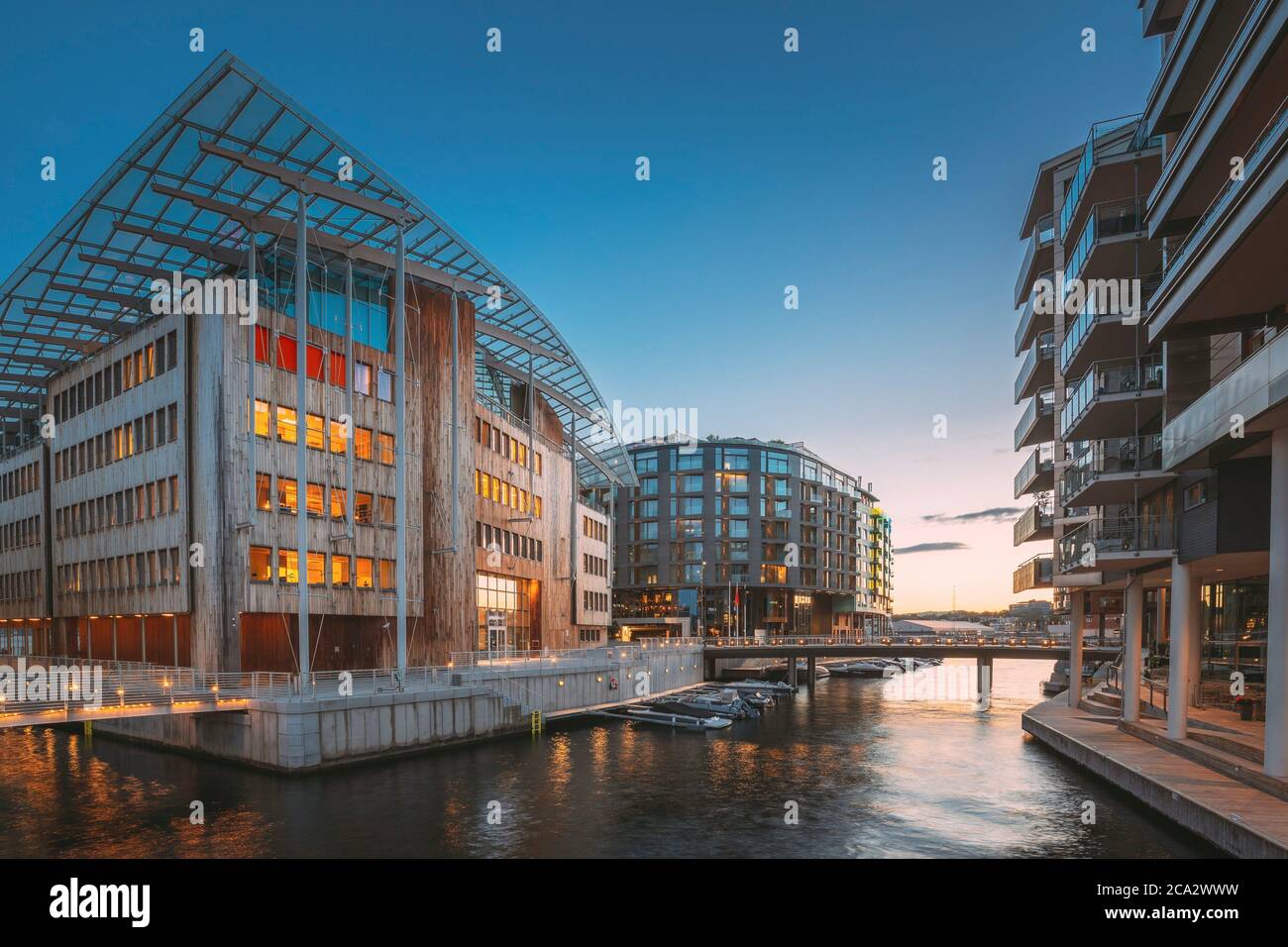 Oslo, Norway. Night View Embankment And Residential Multi-storey Houses In Aker Brygge District. Summer Evening. Residential Area Reflected In Sea Stock Photo