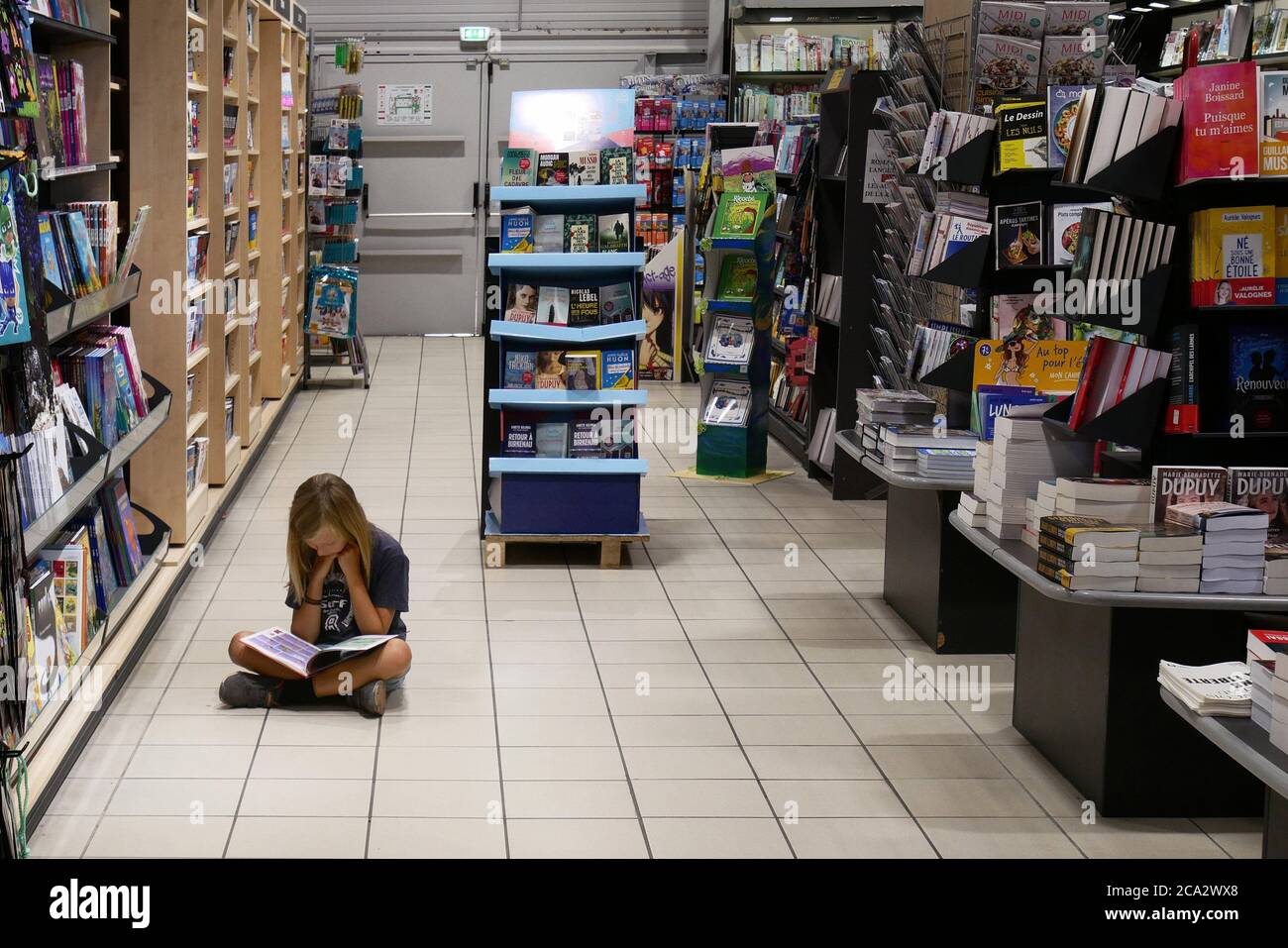 A young girl is fascinated by a book and reads it on the floor of a supermarket Stock Photo