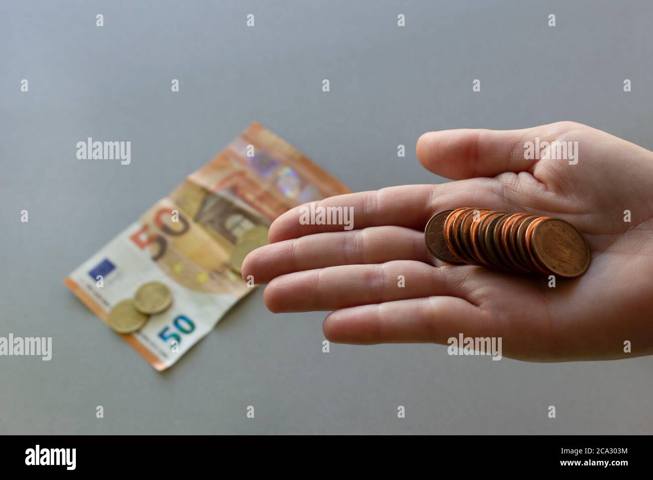 Euro coins in young woman hand.Banknote and more coins on back ,isolated grey background.Saving money and financial crisis concept. Stock Photo