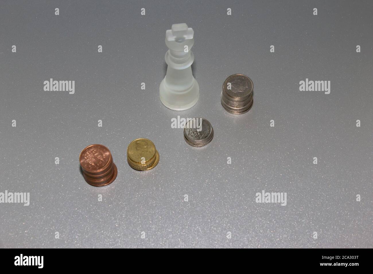 Top view of coins stacks,diferent sizes and colors with chess king piece on grey background.Saving money crisis,business and banking concept. Stock Photo