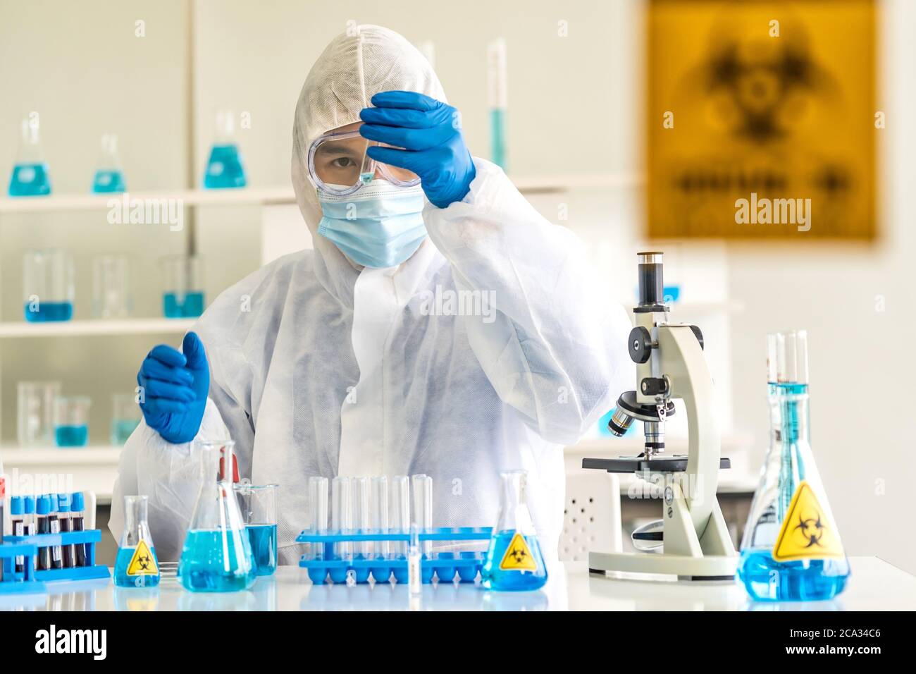 Scientists hold test tube and examine for his research and develop vaccine for coronavirus covid-19 pandemic in Laboratory room with caution signage. Stock Photo