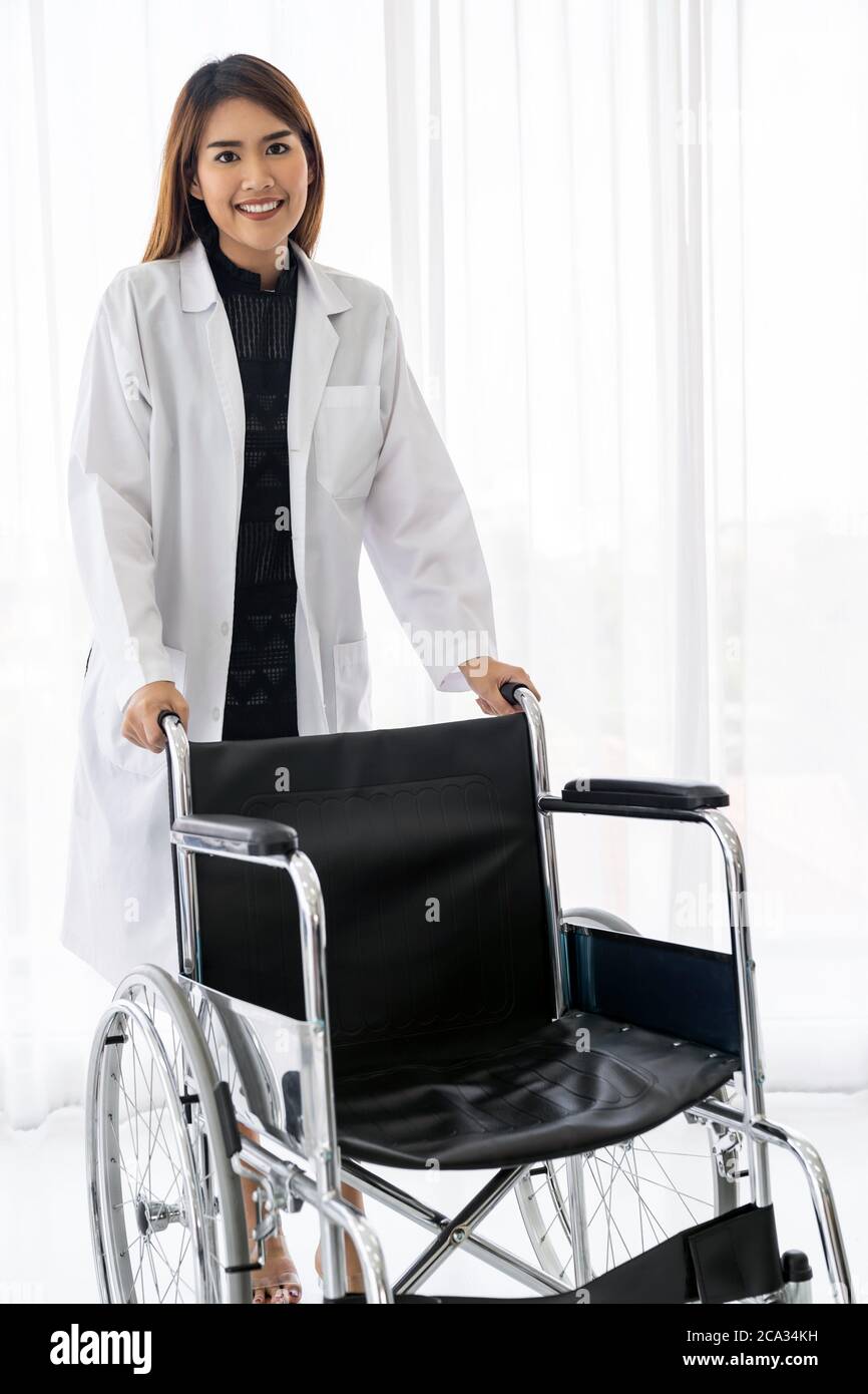 Portrait of confident female doctor medical professional holding wheelchair examination room in hospital clinic. Stock Photo