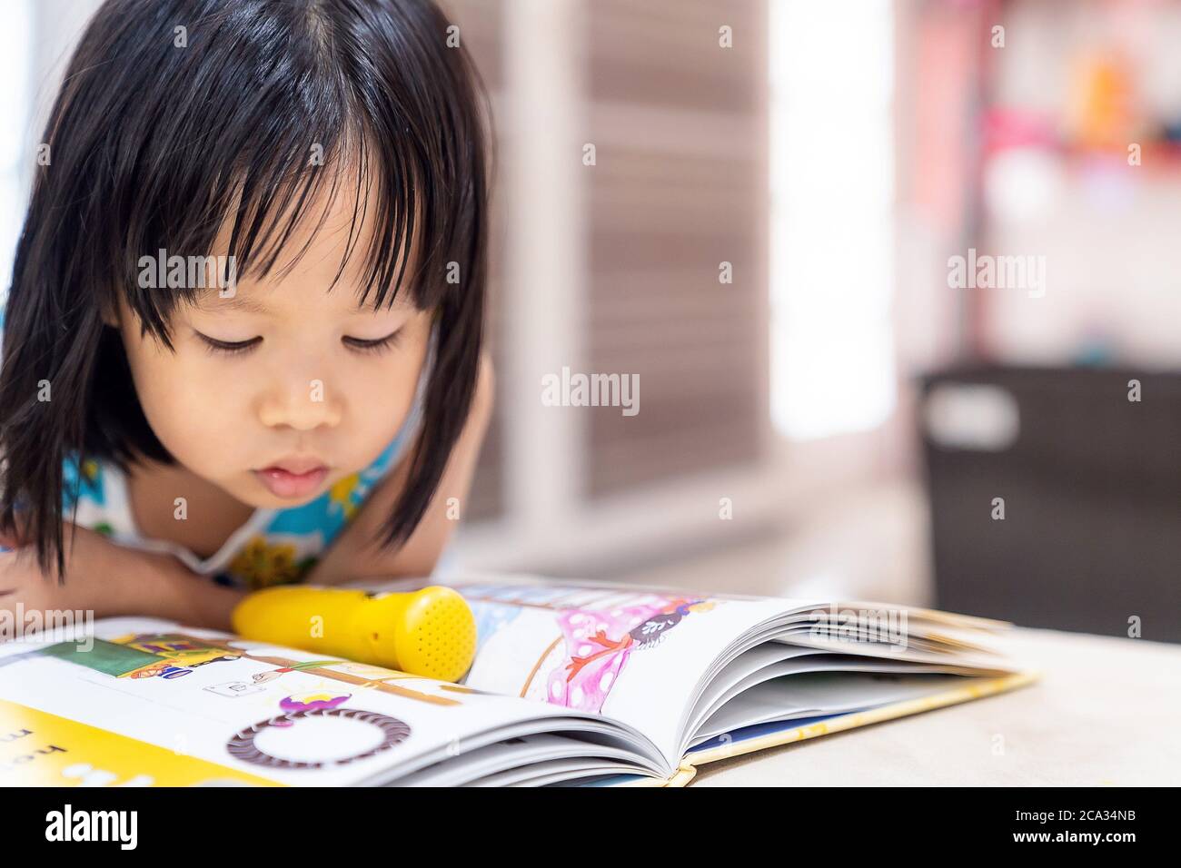 Asian girl child reading interactive book in living room at home as home schooling while city lockdown because of covid-19 pandemic across the world. Stock Photo