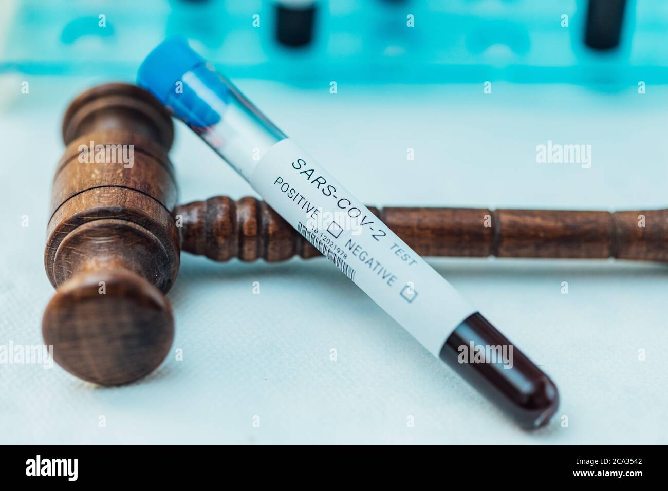 Test tube with blood to do COIVD test supported by judge's gavel. Stock Photo