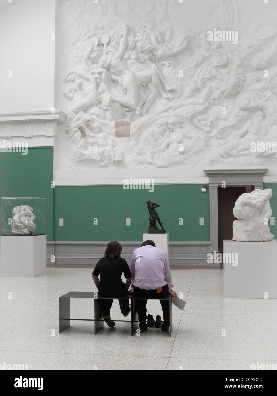 Boots off and swinging feet as two people look at a tumultuous frieze with patched hand and face elements, Antwerp, Belguim. Stock Photo