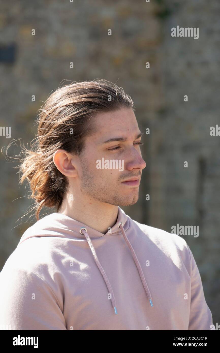 Sunshine highlights the texture of a youth´s man bun while he is lost in thought before Carcassonne Citadel, Occitanie, France. Stock Photo