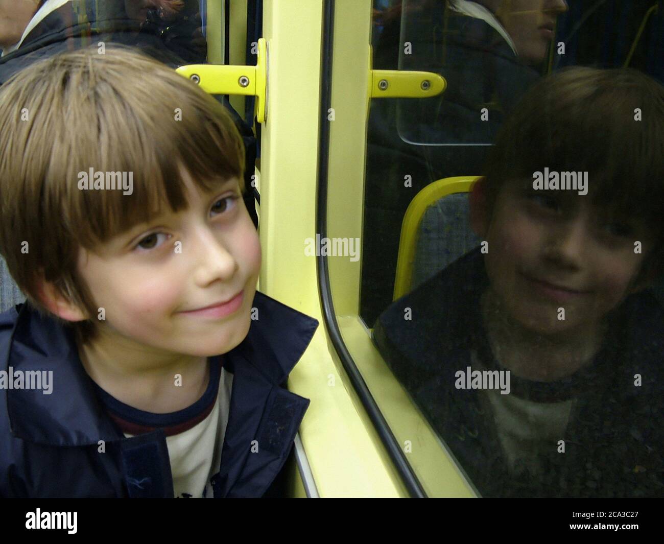 Young boy's serene smile is reflected back at him in the window of the merto train in Zurich, Switzerland, to make him a twin. Stock Photo