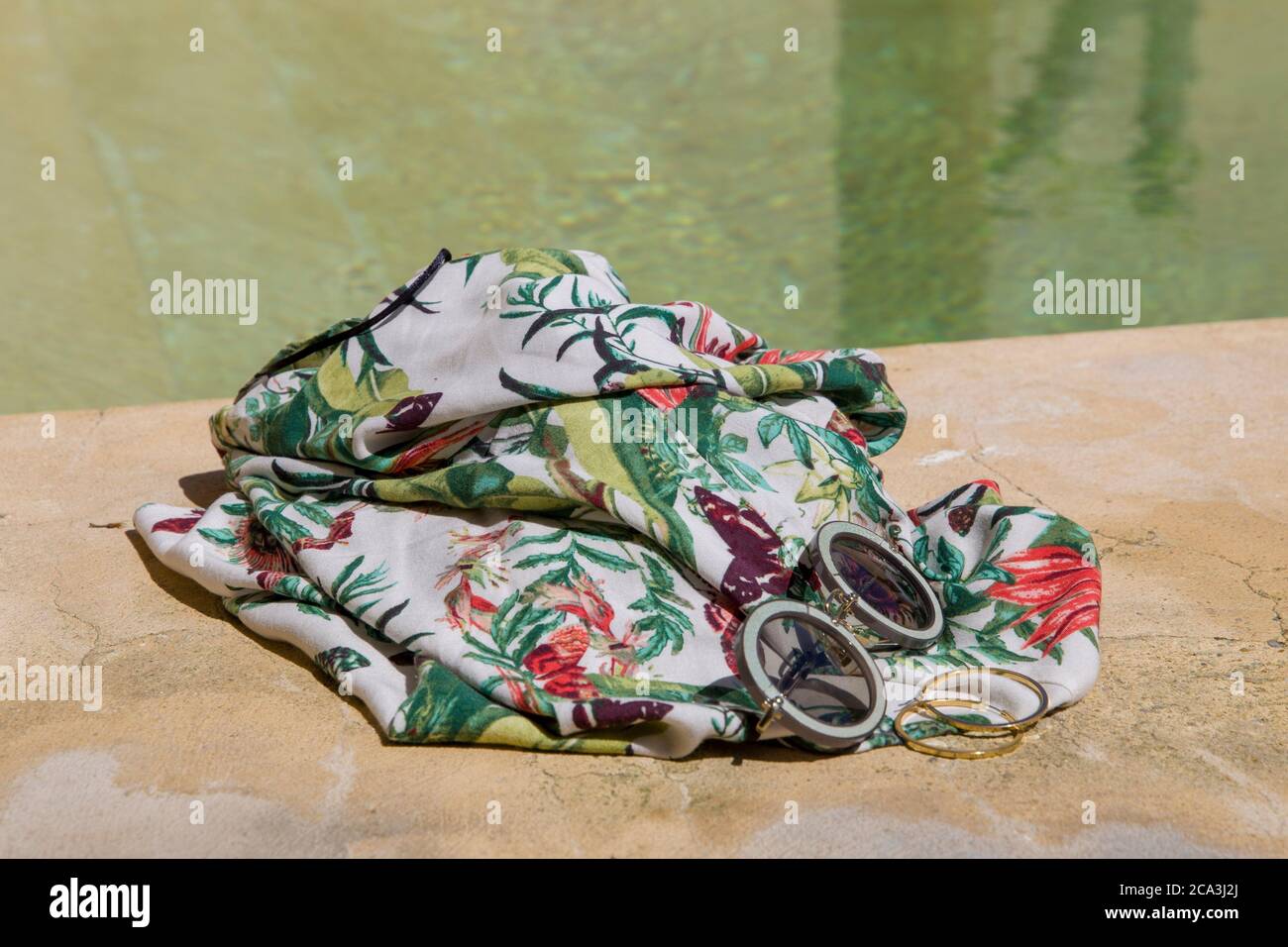 Sunglasses and tropical dress on the edge of a swimming pool. Summer concept with copy space. Stock Photo
