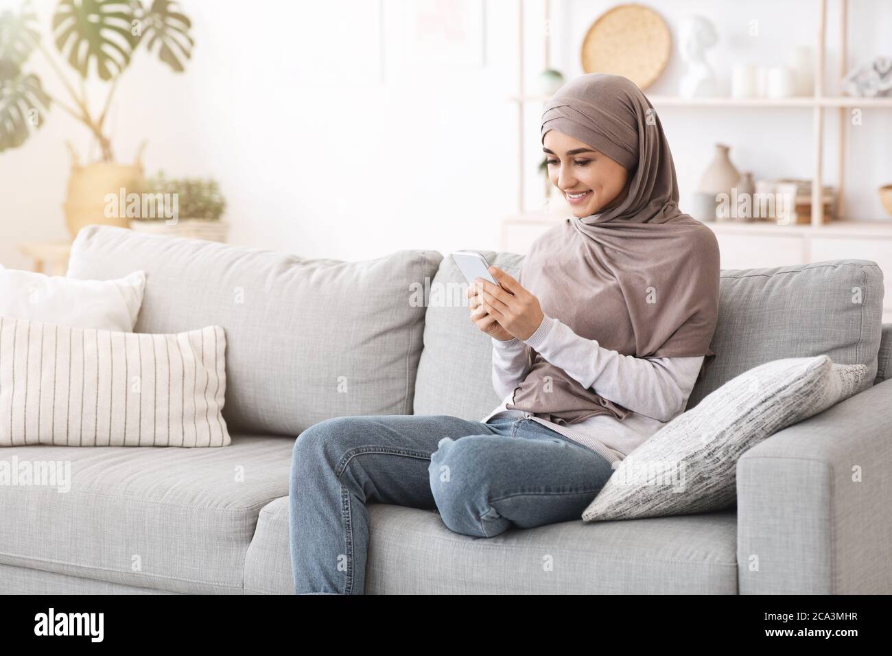 Modern Muslim Girl Using Smartphone At Home While Relaxing On Couch ...