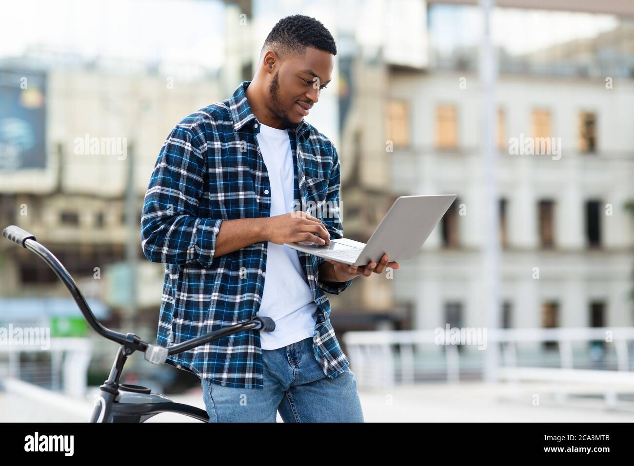 Black man using laptop, standing in downtown with bike Stock Photo