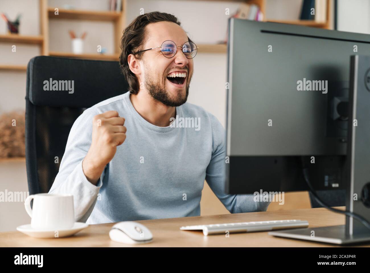 Image of laughing programmer man making winner gesture while working with computer in office Stock Photo