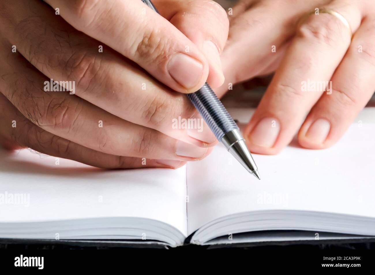 The right hand of a man writing with a pen on a notebook with blank pages. Journalistic or creative activity. White pages. Stock Photo