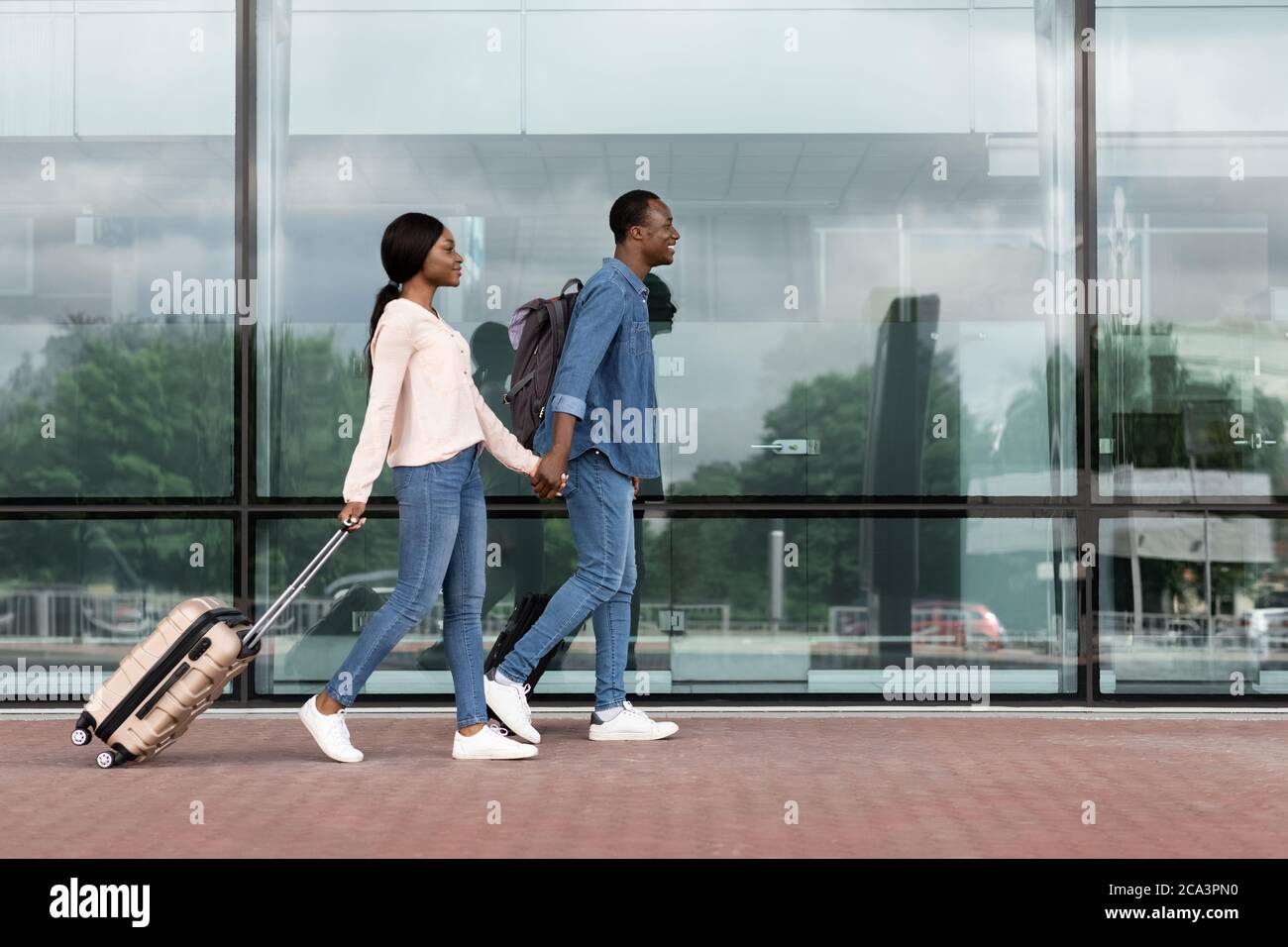 Ready for travel. Happy black couple walking with suitcases near ...