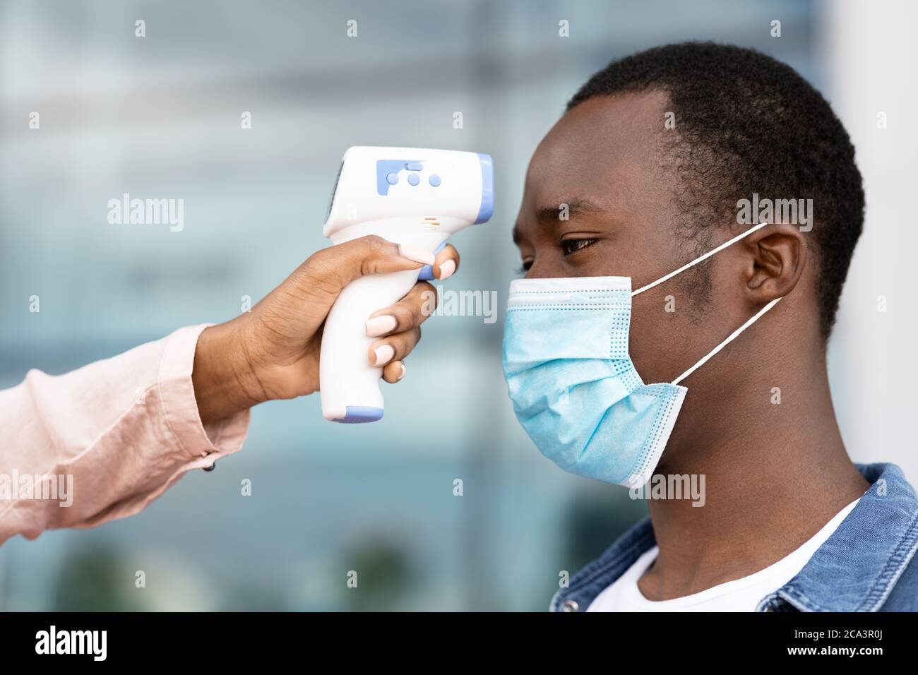 Security Checking Body Temperature With Electronic Thermomether For Black Man In Airport Stock Photo