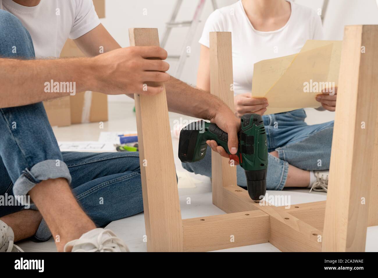 Close-up of unrecognizable man sitting on floor and using screwdriver while assembling table with wife Stock Photo