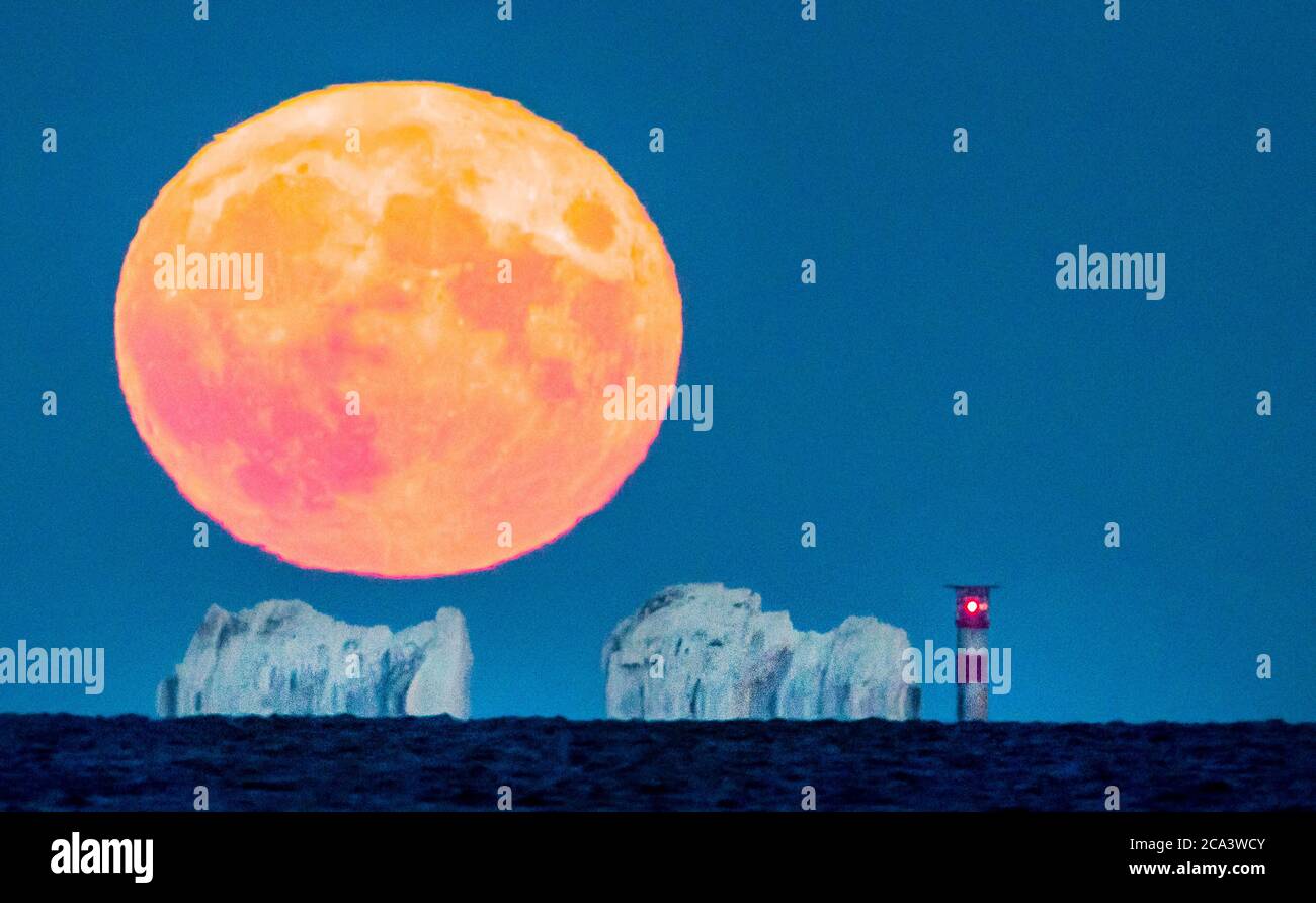 The Needles, Isle of Wight. 3rd August 2020. UK Weather. The full Sturgeon Moon fills the sky above The Needles on the Isle of Wight, dwarfing the 31 metre high lighthouse. Credit Stuart Martin/Alamy Live News Stock Photo
