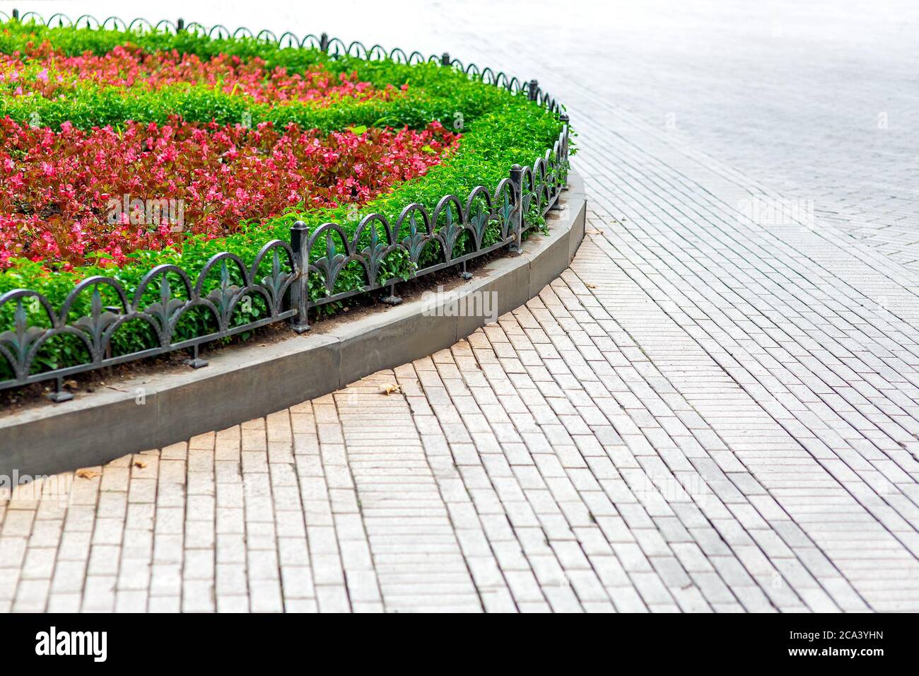 pedestrian pavement of tiles and a flower bed planted ornamental plants  with fenced border with an iron fence, close up street landscape Stock  Photo - Alamy
