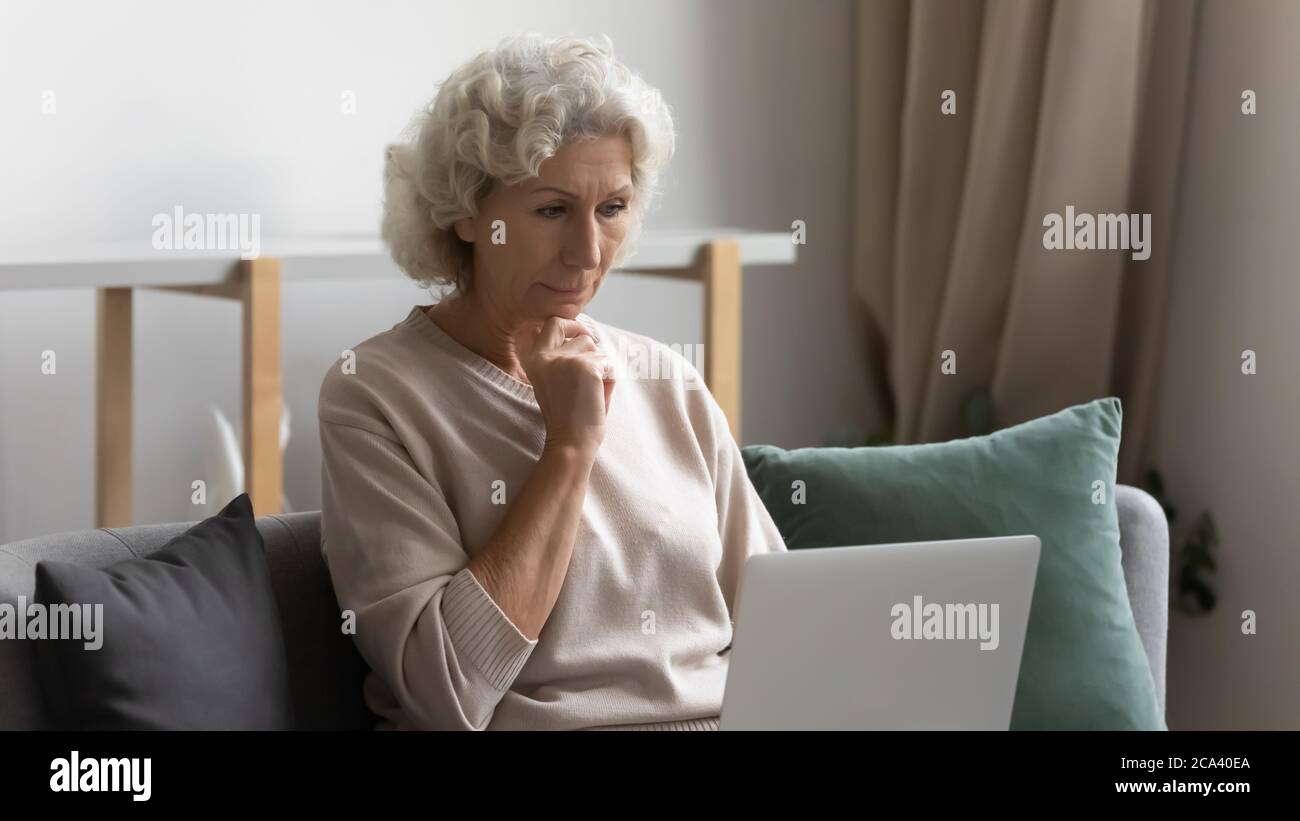 Elderly woman looking at laptop screen feels bewildered Stock Photo