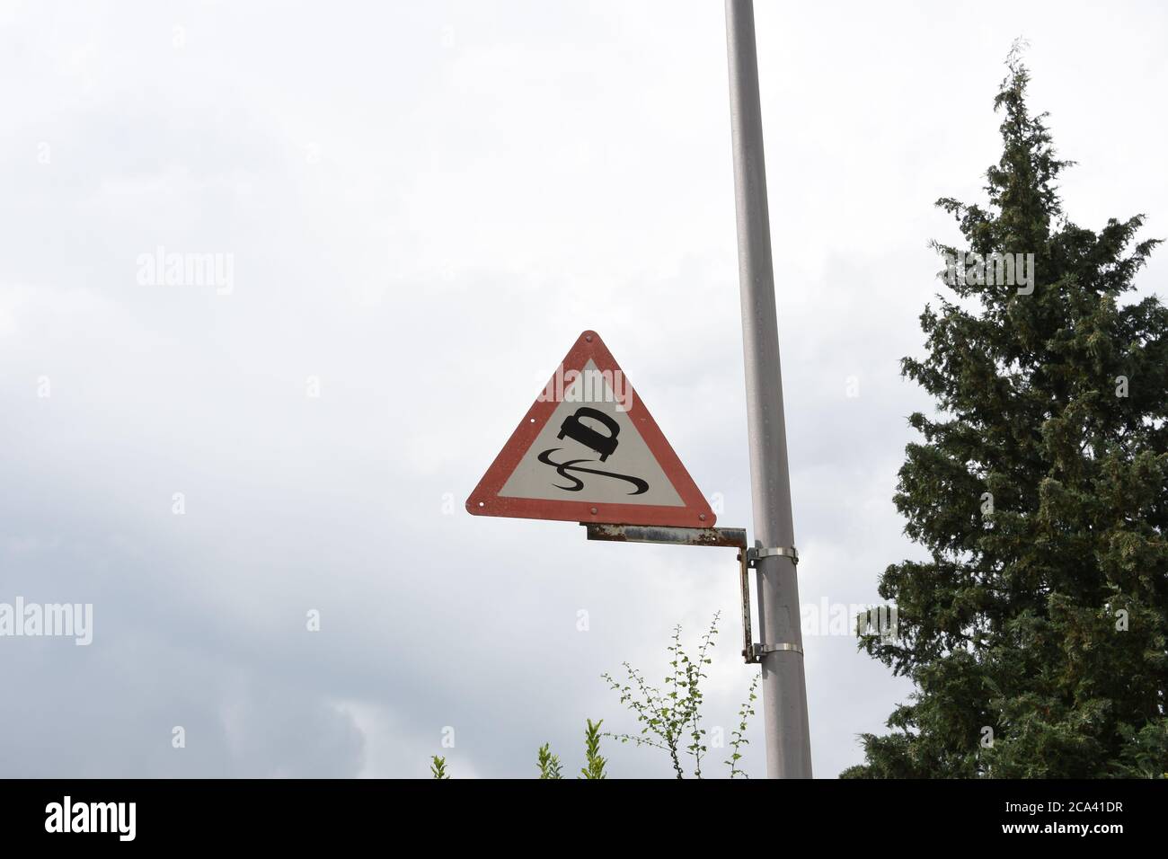 Car Traffic sign Skid Driving Road traffic safety attached to aluminium bar against rainy overcast sky and near a tree in Switzerland countryside. Stock Photo