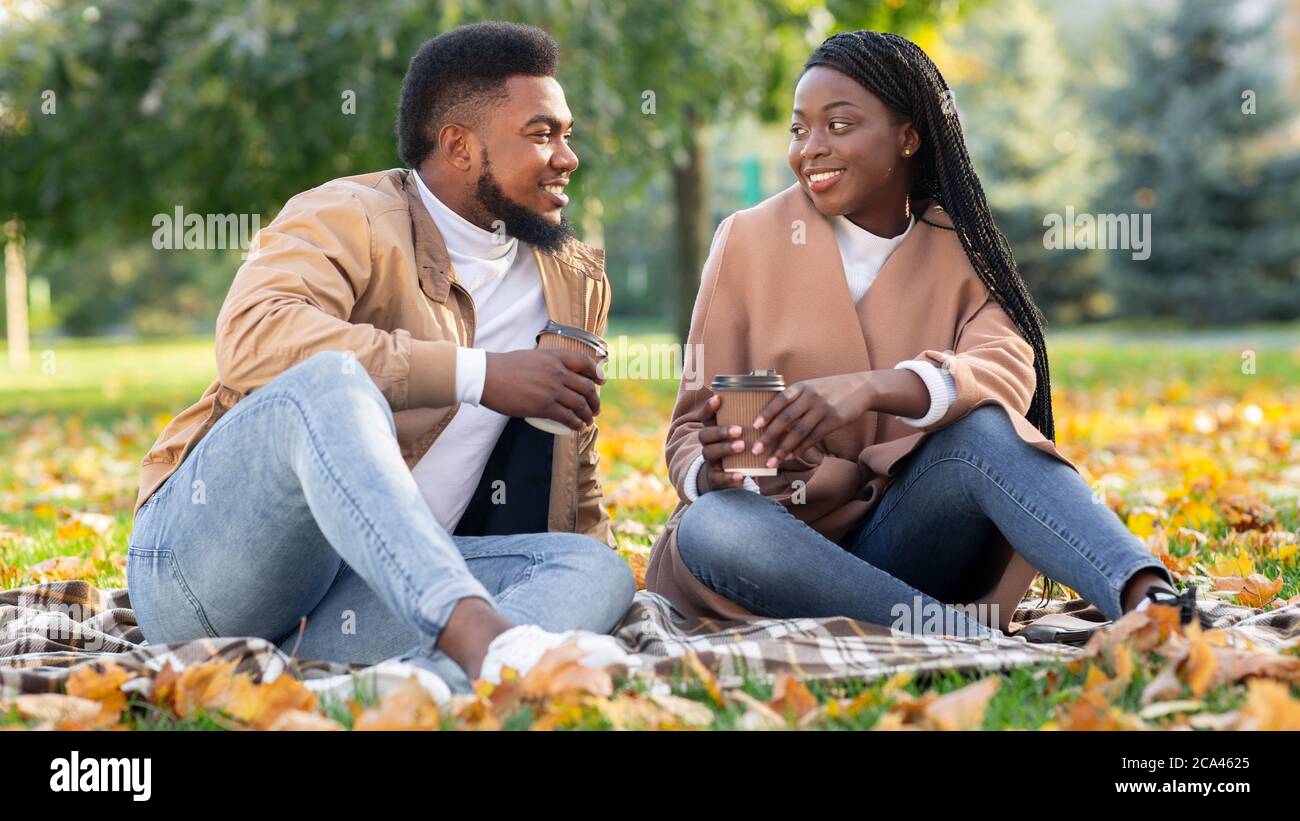 Black couple sitting on picnic in autumn park and drinking coffee Stock Photo