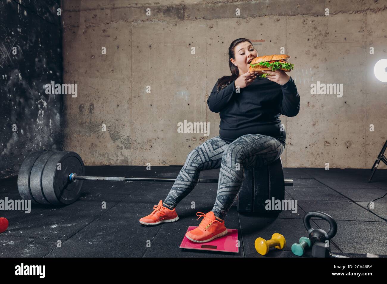 hungry woman cannot overcome the temptation. copy space. offense. fit obese woman eating hamburger aftre training . madness Stock Photo
