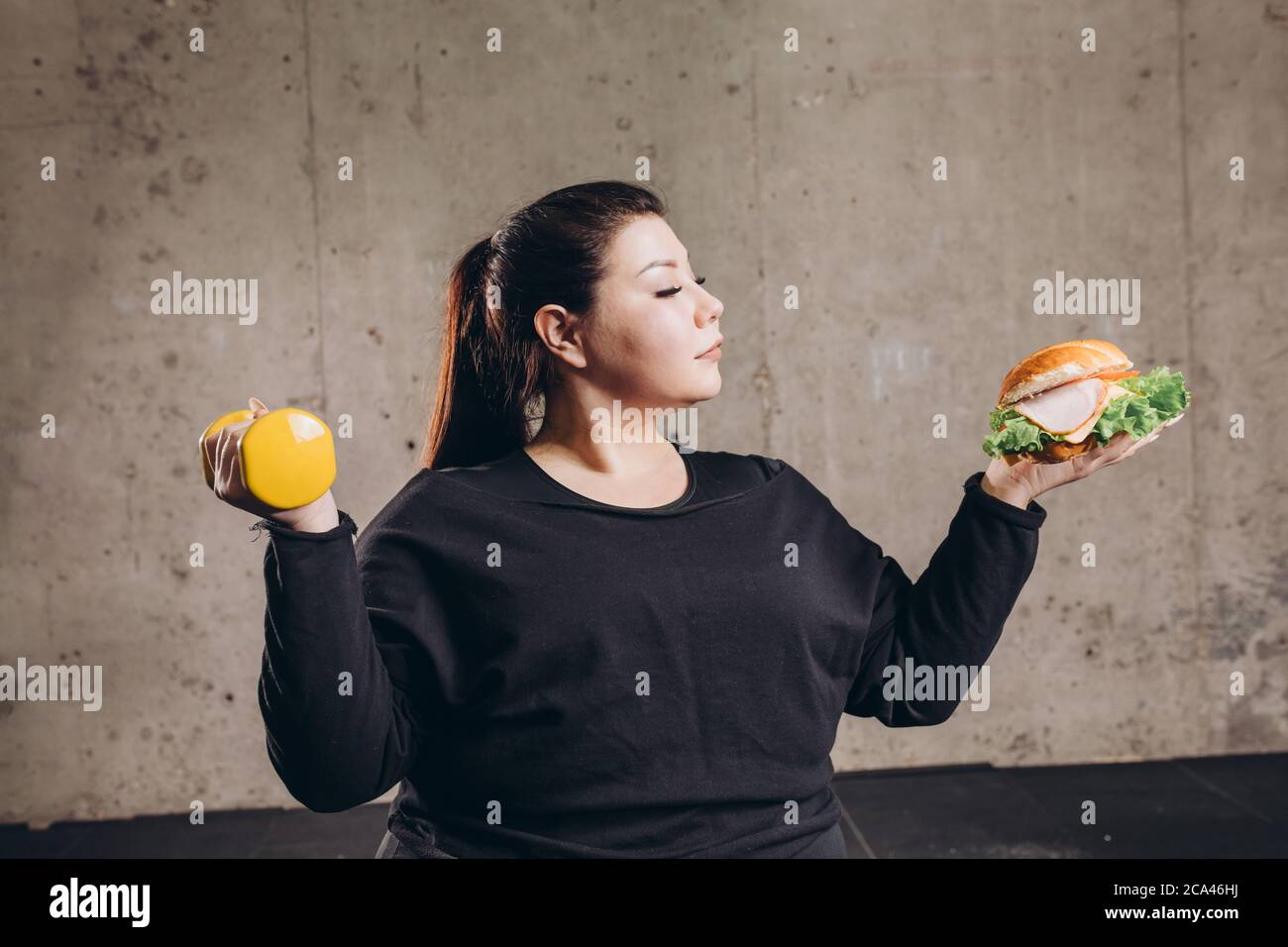 Obese man holding dumbbell eating burger, refusing from doing sport, addiction. close up photo Stock Photo