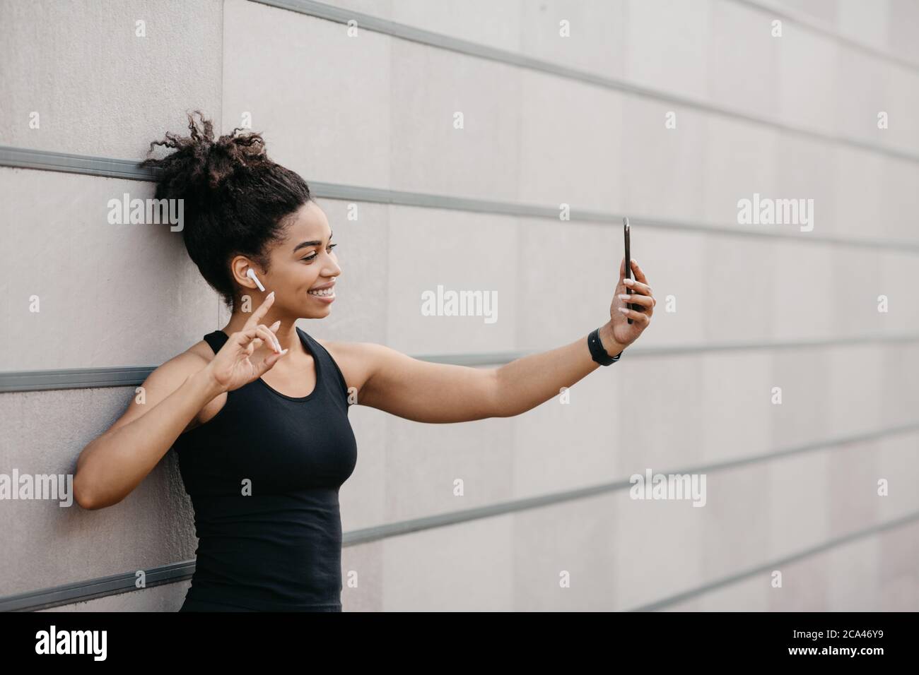 Sports blogger on street workout. Happy girl with fitness tracker makes selfie on smartphone Stock Photo