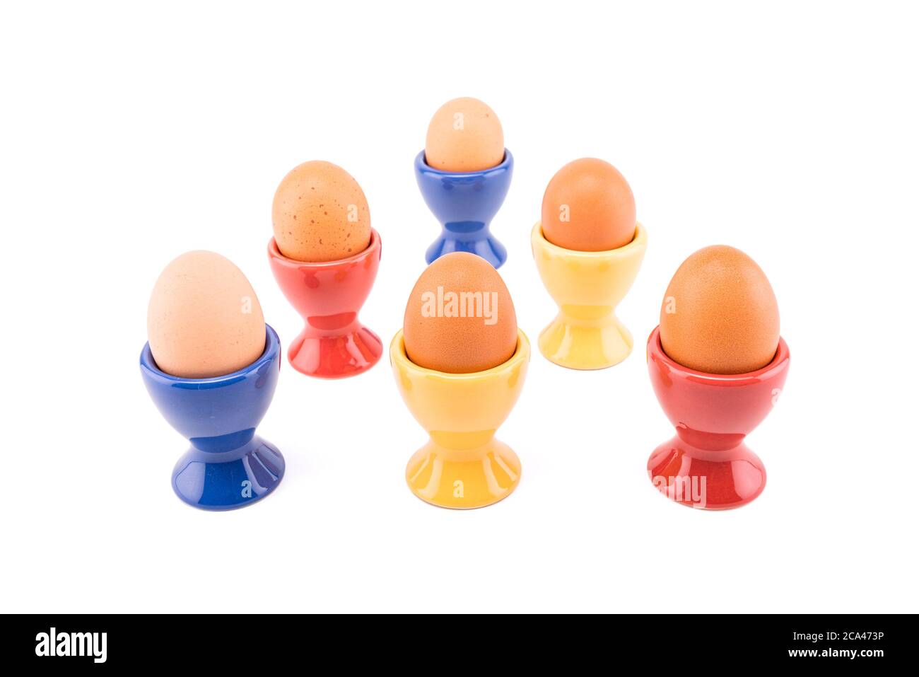 Six ceramic color egg cups with brown eggs. Stock Photo