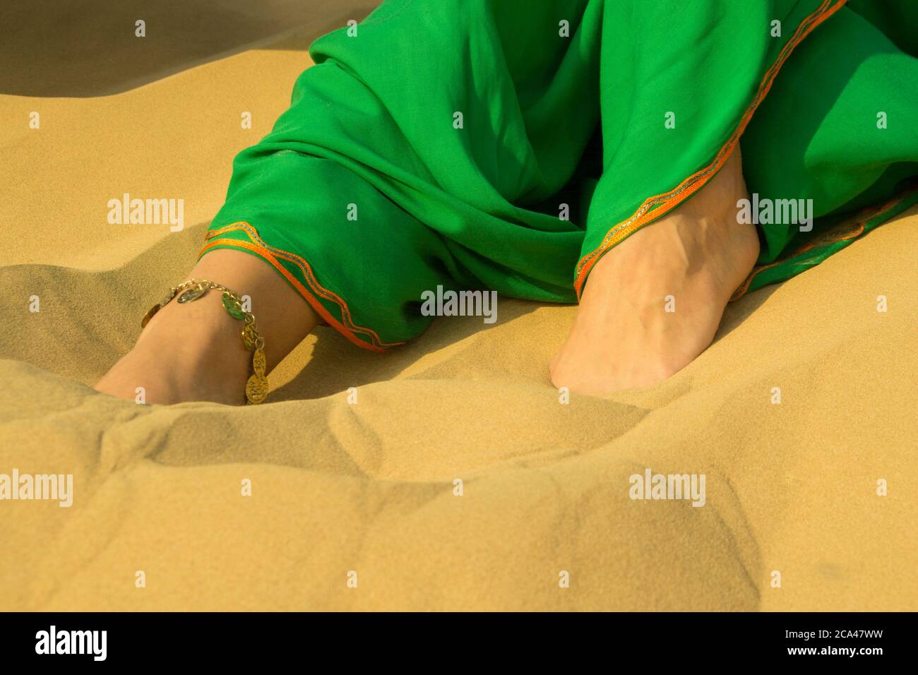 Woman's feet in the desert wearing a green dress and jewellery in her foot Stock Photo