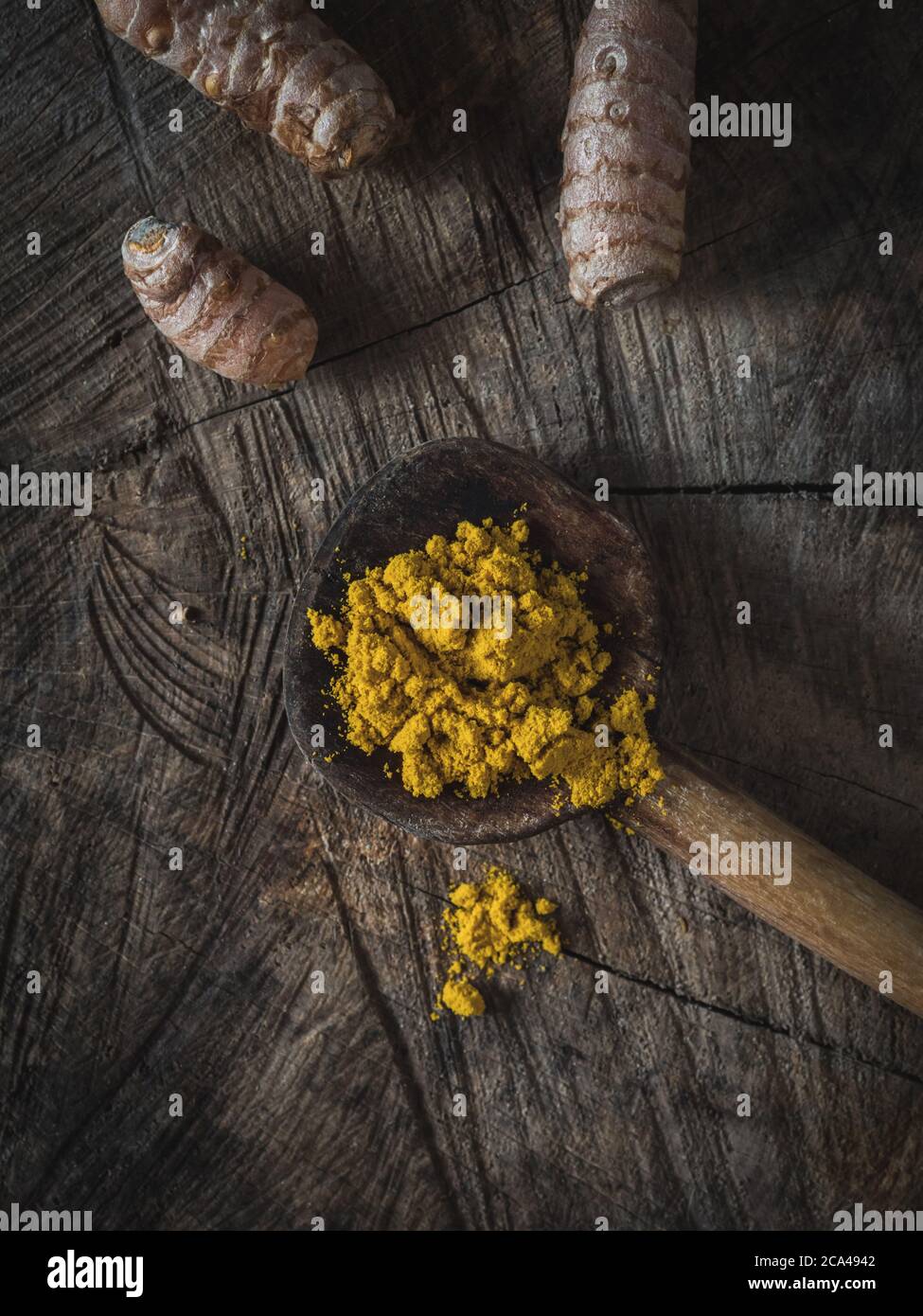 Turmeric (curcumin, Curcuma Longa Linn), powder and rhizome on wooden ladle and vintage wooden table. Overhead shot. Stock Photo