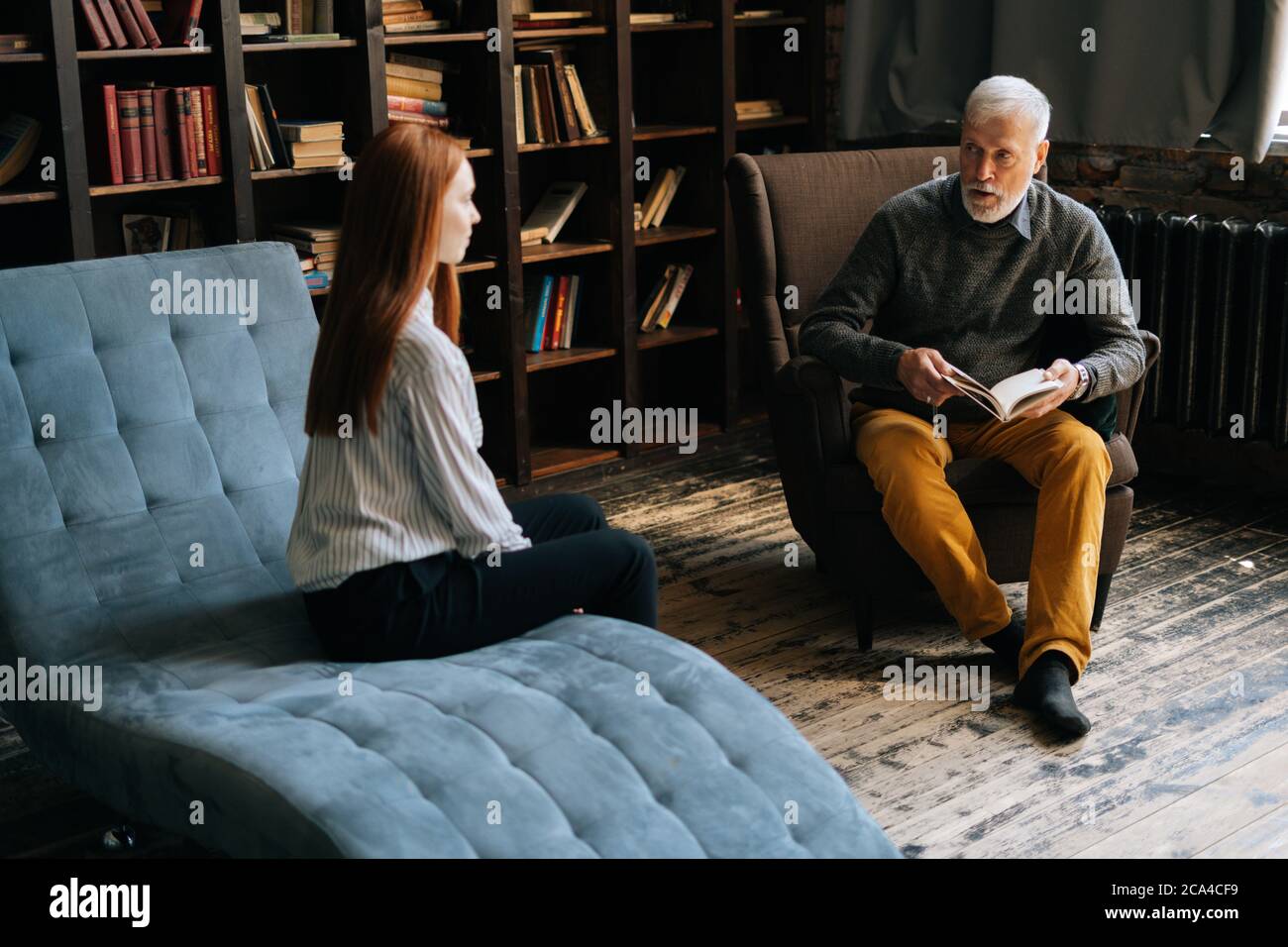 Redhead young woman listening to older psychologist doctor explaining treatment. Stock Photo
