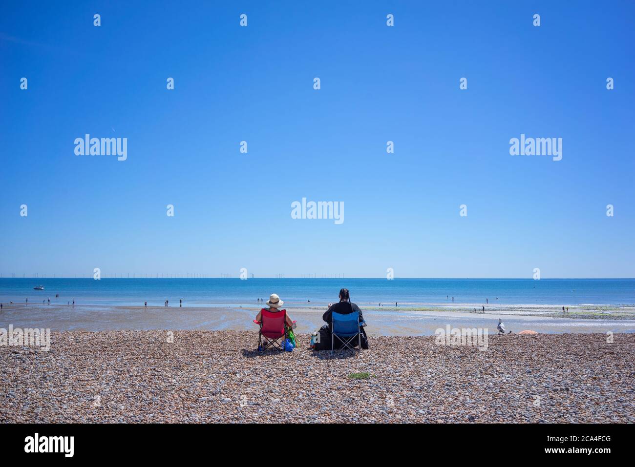 Coastal view with two elderly people sitting on the beach looking at ...