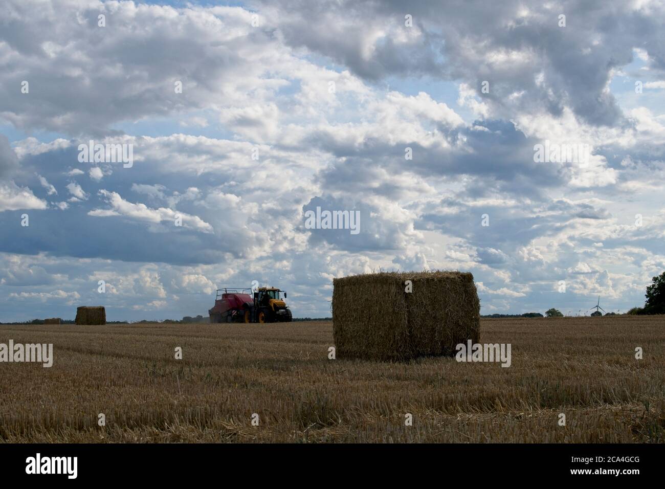 Baling following the combine harvester Baling following the combine harvester. Tractor towing bailer ejecting bale onto the ground Moving into picture Stock Photo