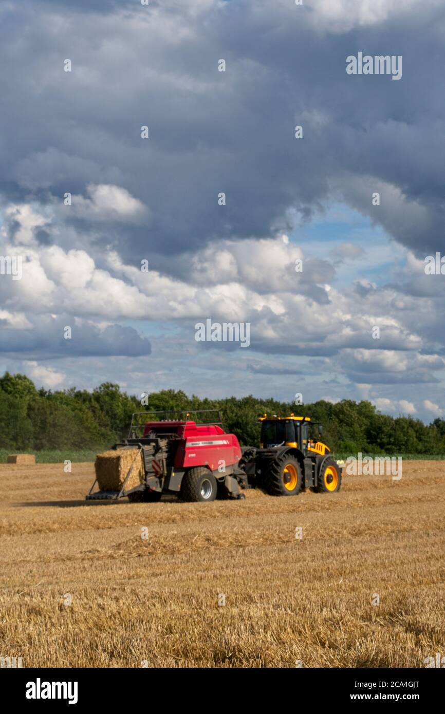 Baling after the harvest Tractor towing bailer ejecting bale onto the ground Moving left to right Sunny cloudy sky Image sequence Portrait format Stock Photo