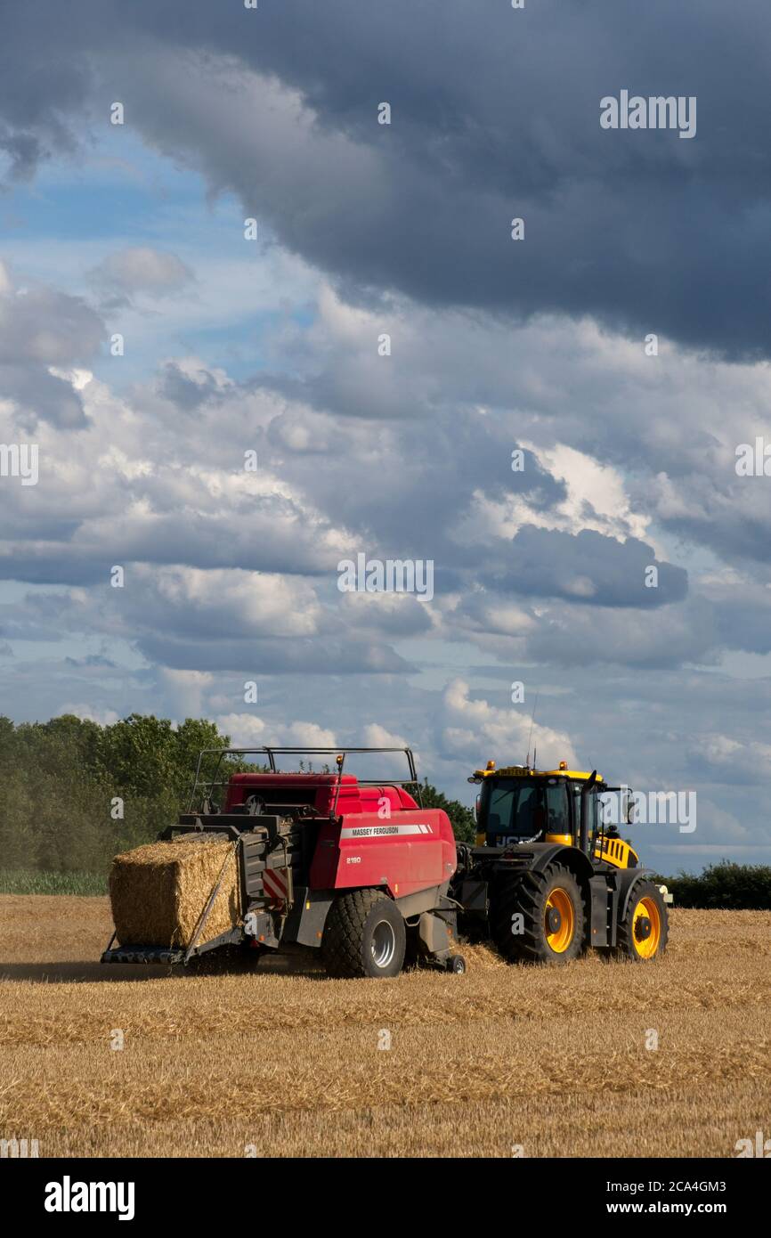 Baling after the harvest Tractor towing bailer ejecting bale onto the ground Moving left to right Sunny cloudy sky Image sequence Portrait format Stock Photo