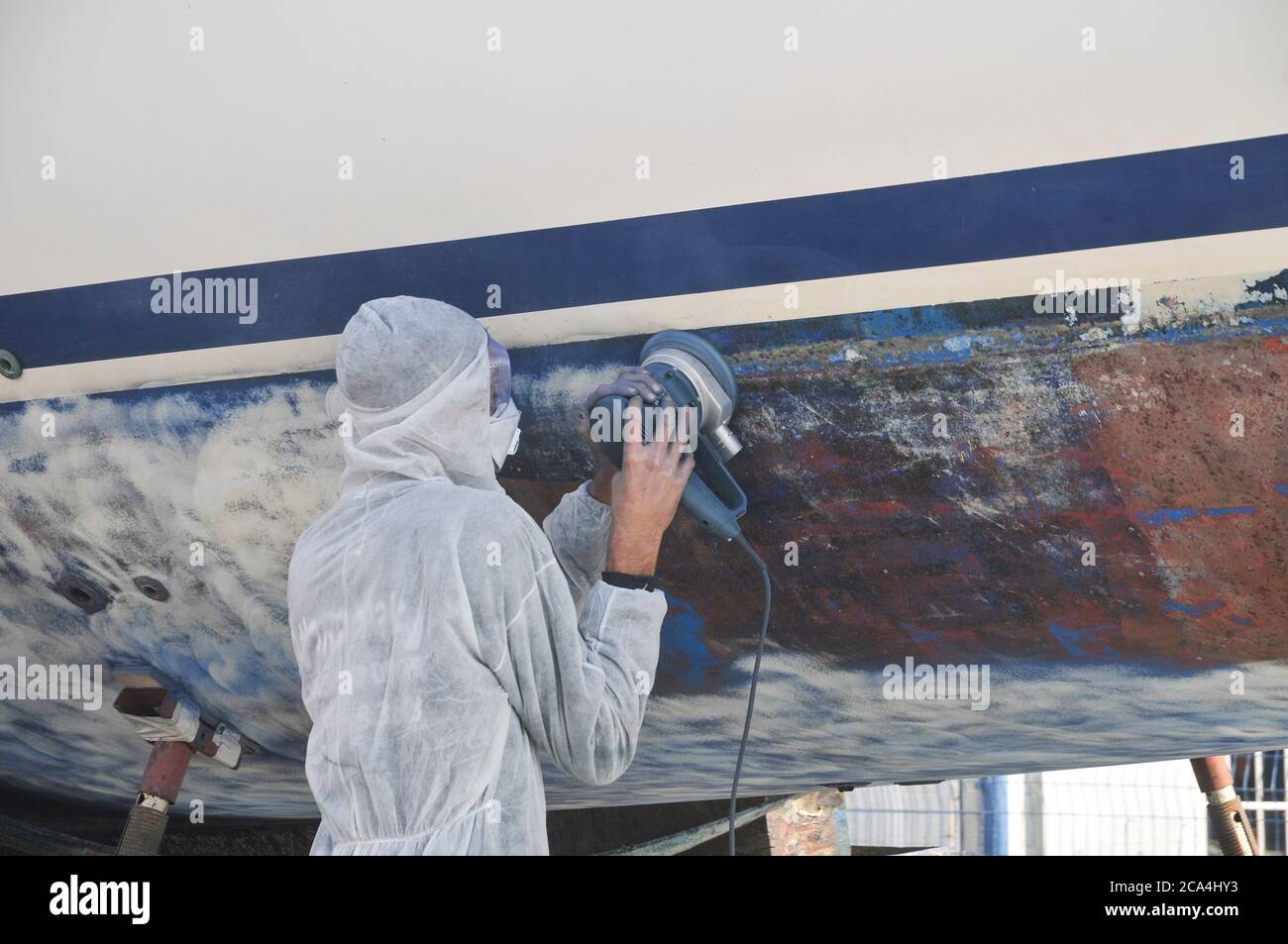 Boat maintenance. Worker with safety gear uses a power tool to scrape