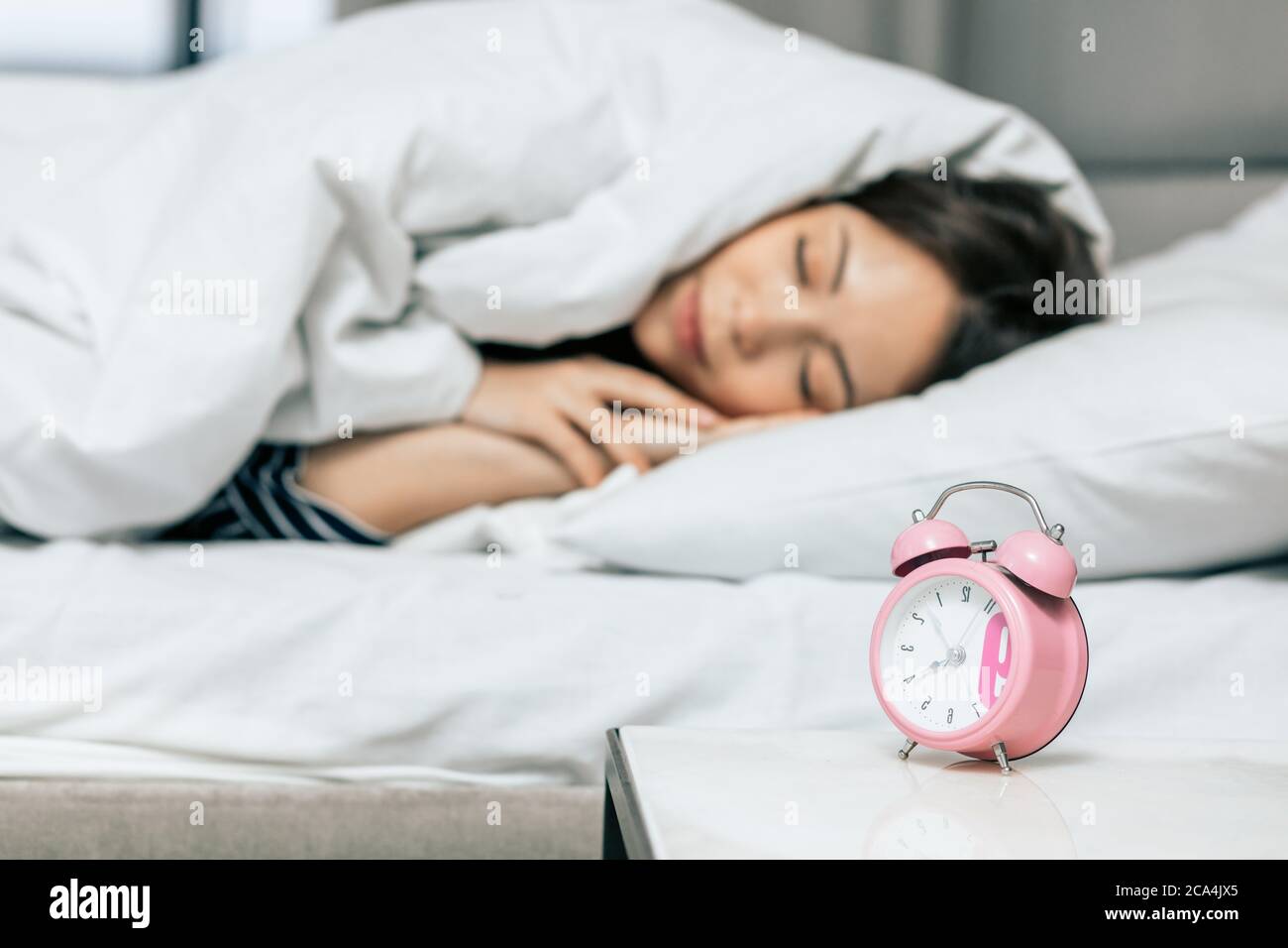 focus on pink alarm clock, sleeping relaxed awesome girl on blurred