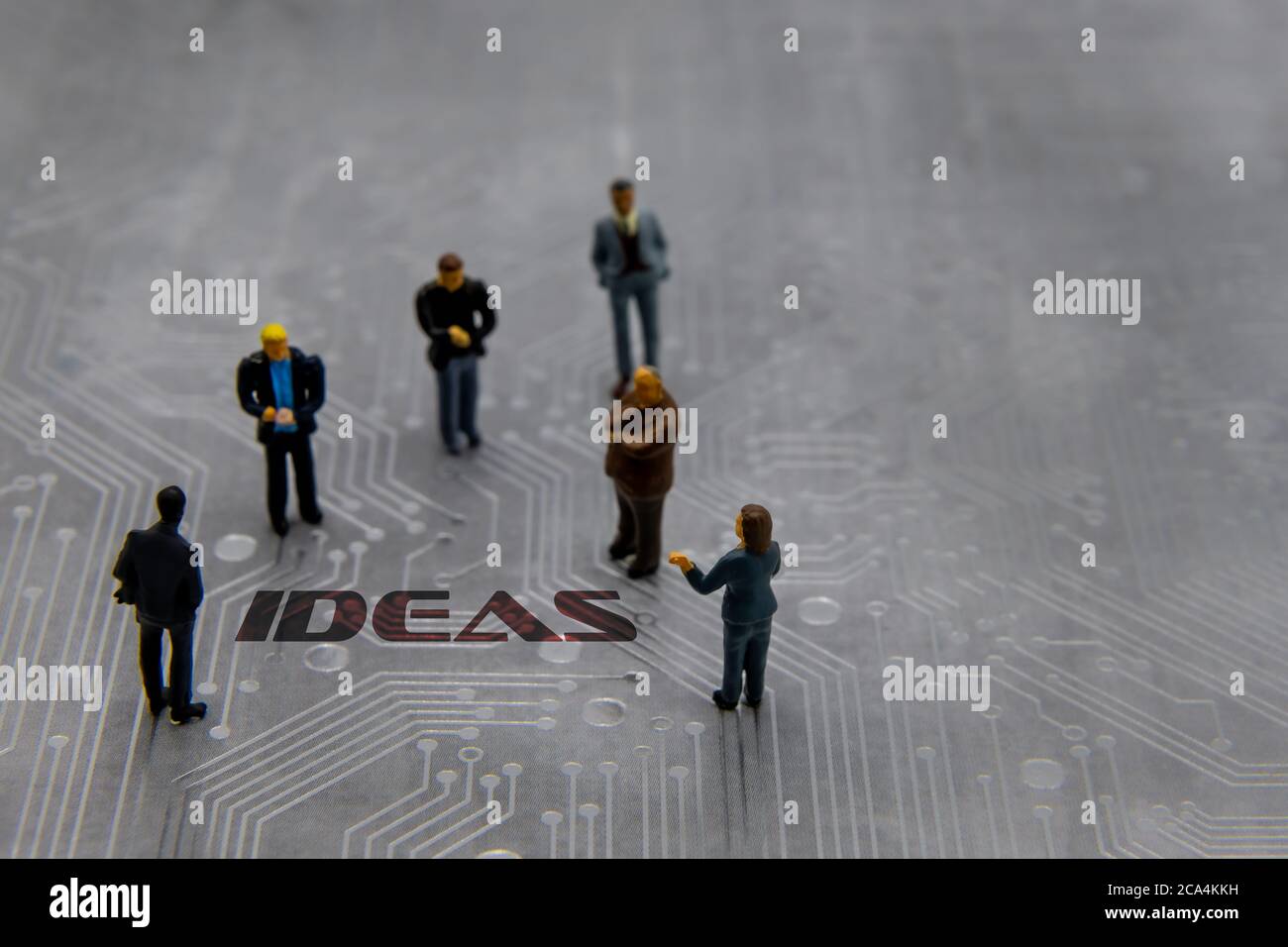 Miniature figurines posed as business people in a meeting over abstract futuristic circuit board with text Ideas Stock Photo