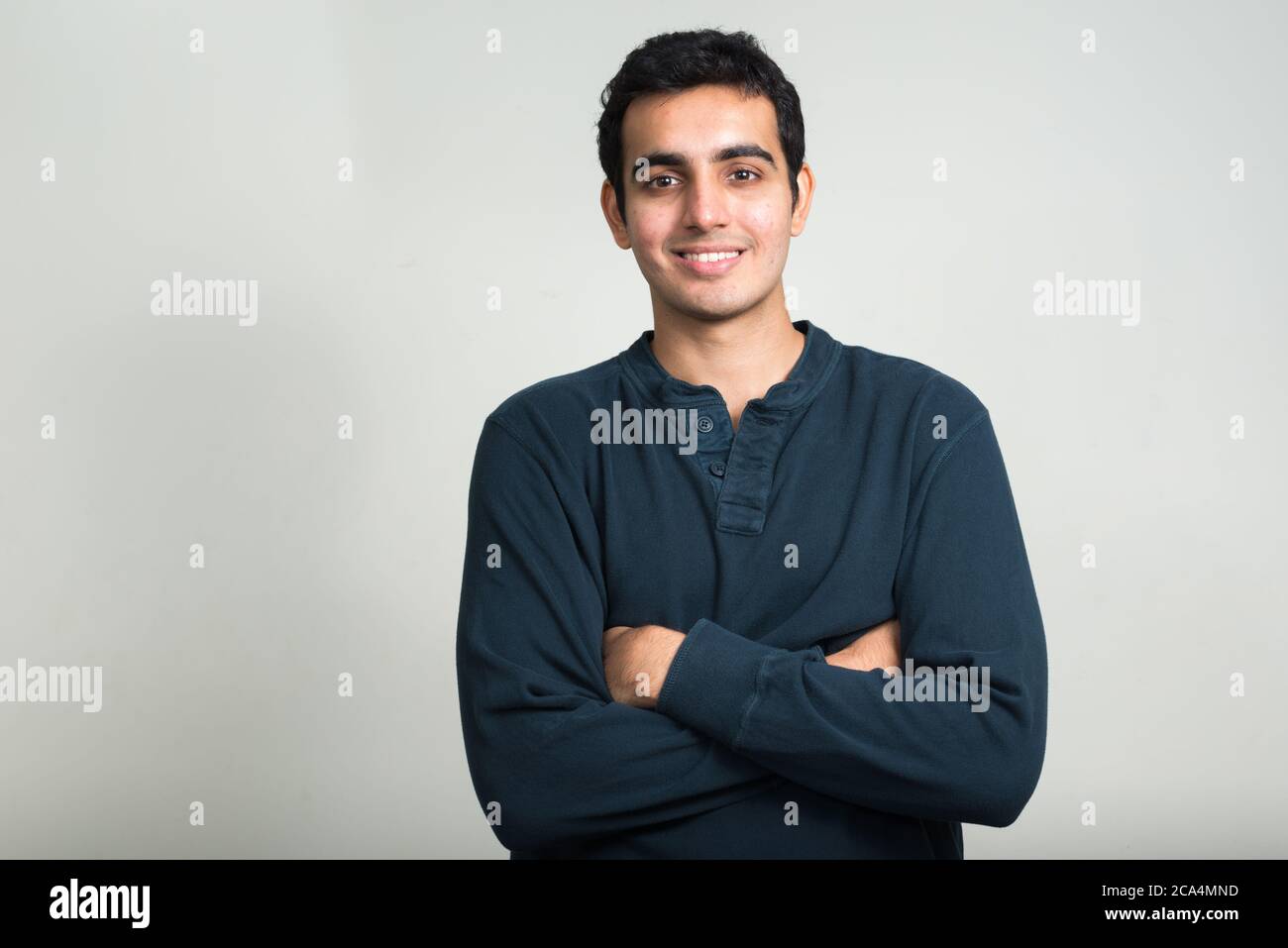 Portrait of happy young handsome Indian man smiling with arms crossed ...