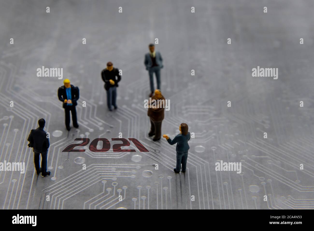 Miniature figurines posed as business people in a meeting over abstract futuristic circuit board with text year 2021 Stock Photo