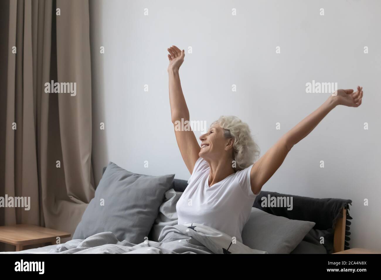 Senior woman sitting in bed feels rested after night sleep Stock Photo